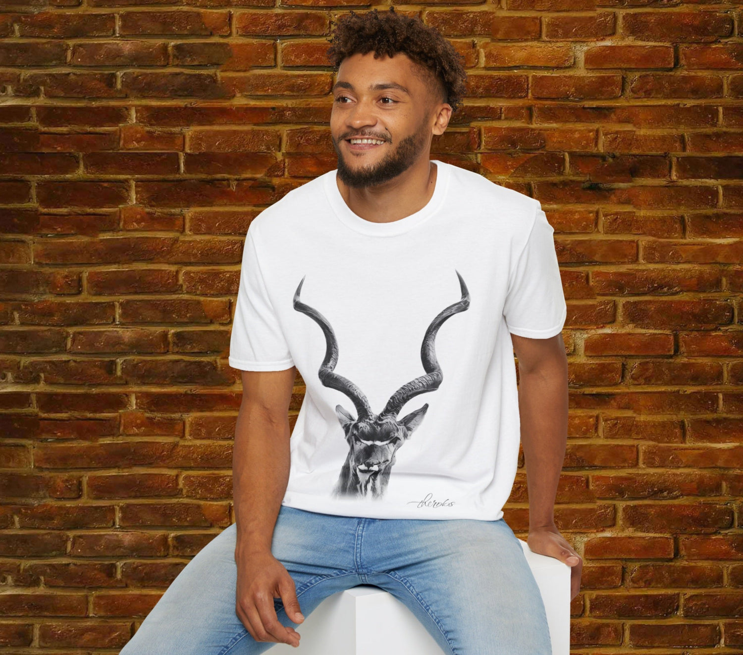 Man wearing a white t-shirt with a graphic design of an animal sitting against a brick wall.
